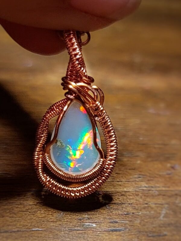 Pendant with opalescent gemstone and copper wire wrapping.